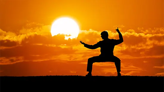 Tai Chi - man standing at sunrise in a tai chi pose